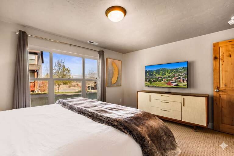 Rest easy in your spacious bedroom with a plush bed, modern TV, and peaceful neighborhood views—your perfect retreat after mountain adventures.