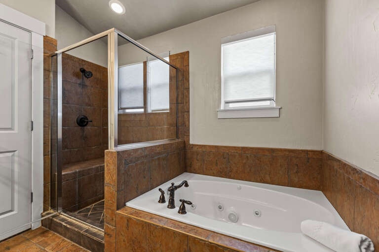 Unwind in your private spa-like bathroom featuring a luxurious jetted tub and spacious walk-in shower. Natural light creates a serene atmosphere perfect for relaxation.