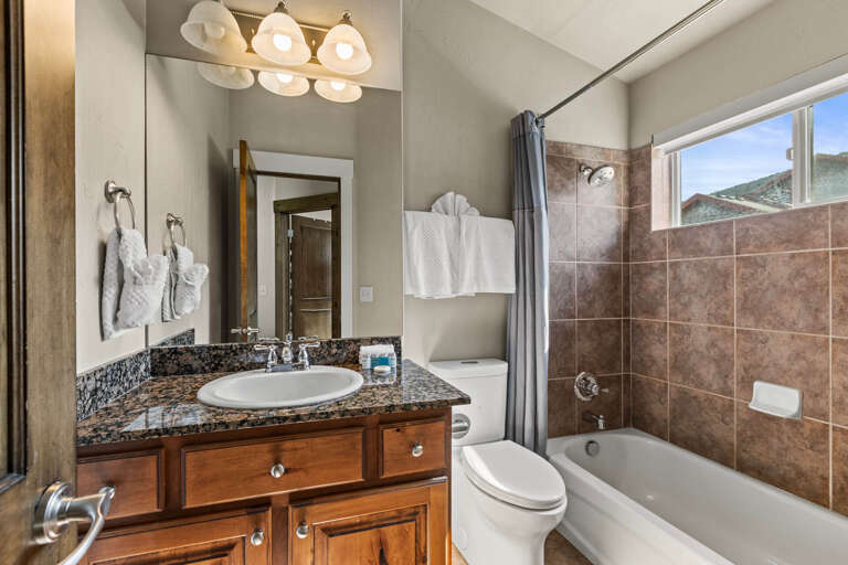 Step into your private bathroom with granite countertops, warm wood cabinetry, and a relaxing tub-shower combo. Fresh towels await you, and natural light brightens your morning routine.