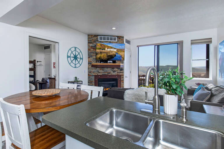 Your open kitchen flows into a cozy living space with fireplace and stunning mountain views through panoramic windows.