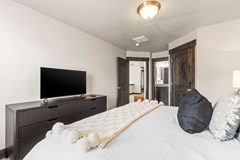Unwind in your peaceful bedroom with plush bedding, modern TV, and stylish storage for a perfect night's rest.