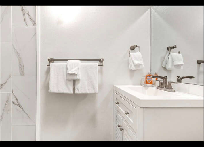 Pamper yourself in this pristine bathroom featuring elegant marble-look tiles and plush white towels awaiting your arrival.