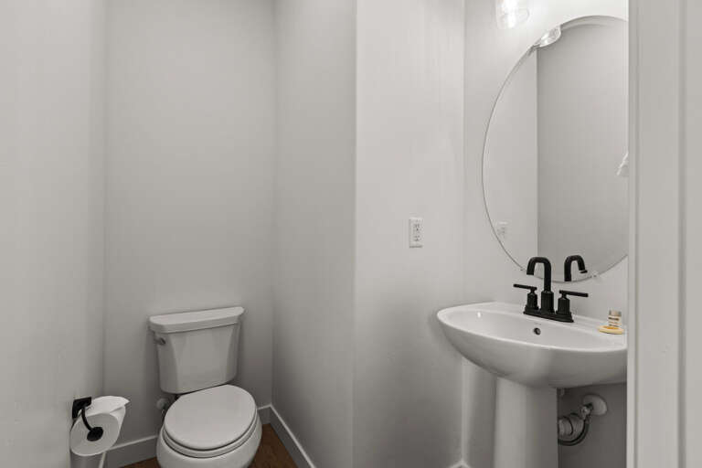 A crisp, modern bathroom awaits your arrival with fresh white fixtures, a stylish round mirror, and matte black faucet—perfectly appointed for your daily rituals.