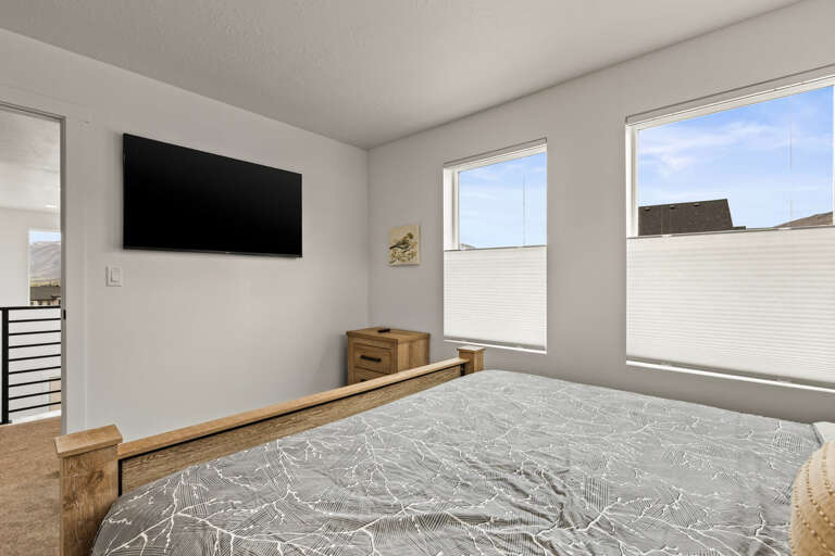 Your bright bedroom features a wall-mounted TV and peaceful windows for restful mornings and cozy evenings.