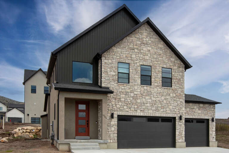 Modern two-story home featuring stunning stone and metal exterior with spacious three-car garage in peaceful neighborhood setting.