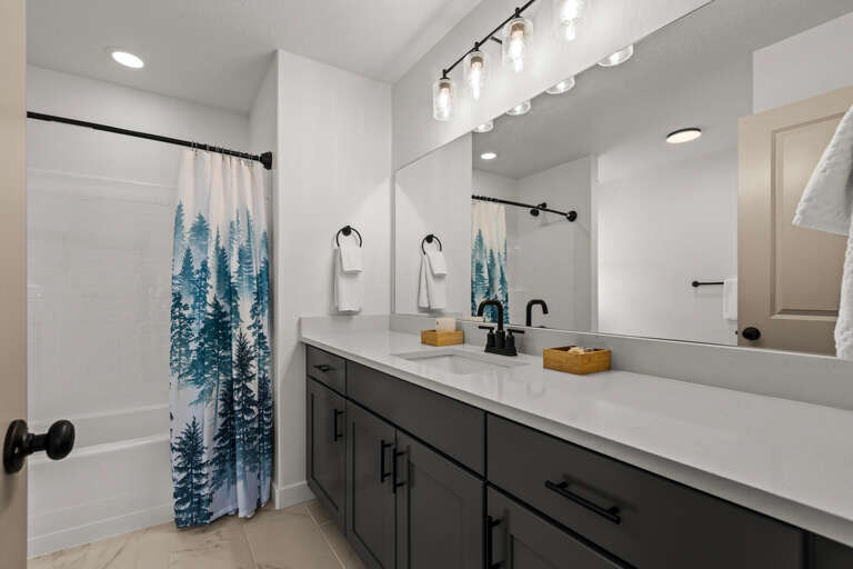 Refresh in your modern bathroom with elegant lighting, granite counters, and a nature-inspired forest shower curtain creating a spa-like retreat.