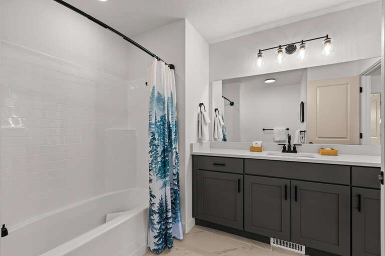 Unwind in your spacious bathroom with crisp white subway tiles, forest-themed curtains, and modern gray cabinetry creating a spa-like retreat.