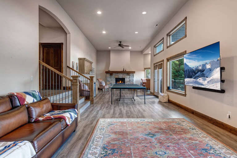Unwind in your spacious living area featuring soaring ceilings, a cozy fireplace, and ping pong—all framed by stunning mountain views through expansive windows.