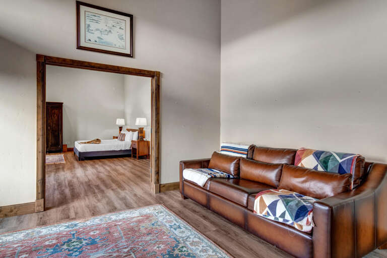 Step into a spacious suite where a warm leather sofa invites you to unwind, connecting seamlessly to a serene bedroom beyond through elegant wood-framed doorways.