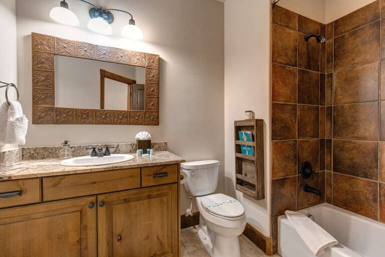 Unwind in your private bathroom featuring warm earth-tone tiles, a relaxing tub-shower combo, and rustic wood accents that create a cozy mountain retreat atmosphere.