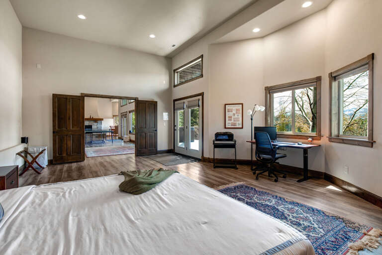 Your bright and airy bedroom offers a peaceful retreat with hardwood floors, vaulted ceilings, and a dedicated workspace overlooking scenic views. Step through the French doors to explore nearby areas.