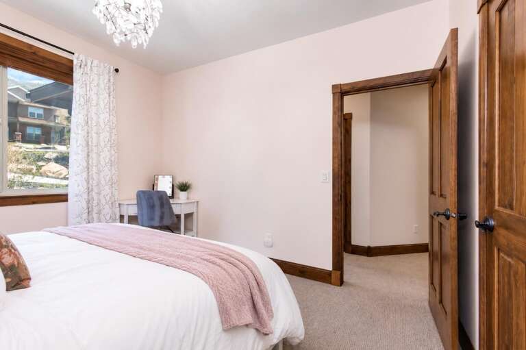 Your peaceful retreat features a plush bed, natural light from the window, a cozy desk nook, and elegant touches like the statement chandelier overhead.