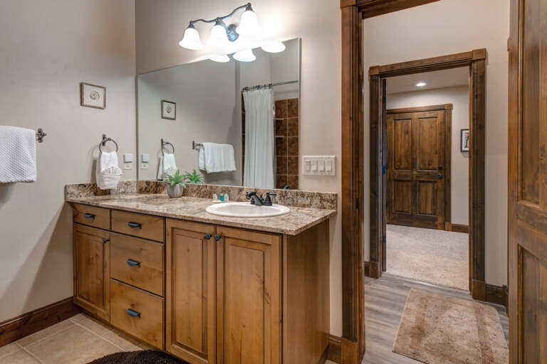 Step into your serene private bathroom with granite countertops, warm wood cabinetry, and soft towels waiting for you. The inviting shower is just steps away for a refreshing start to your day.
