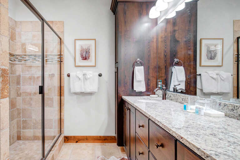 Your private bathroom features a spacious walk-in shower with beautiful tiled walls, elegant granite countertops, and plush white towels waiting for you.