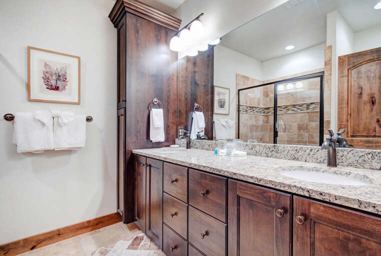 Step into your private bathroom featuring rich wood cabinetry, gleaming granite counters, and a spacious walk-in shower. Fresh towels await your arrival, and thoughtful details create a warm, spa-like atmosphere for unwinding.