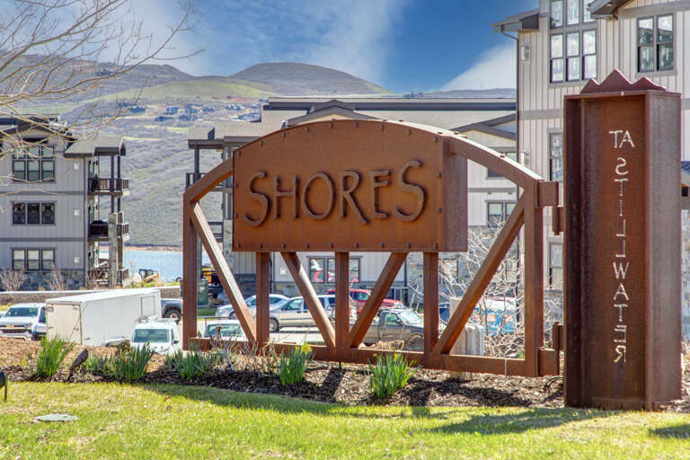 Mountain resort entrance near lakefront and hillside, featuring distinctive architectural signage identifying the property among surrounding residential buildings.