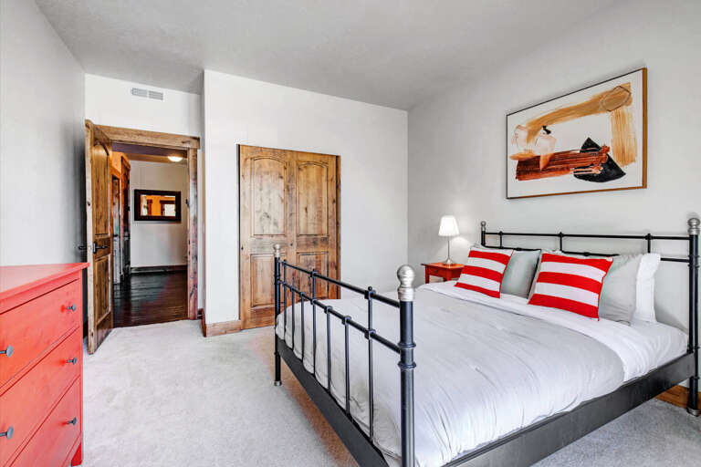 Sink into crisp white linens and cheerful red-striped pillows in your restful bedroom, where rustic wooden doors and vibrant artwork add character to your mountain getaway.