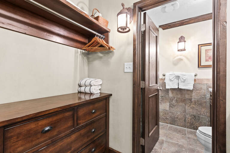 Step into your private retreat, where rustic charm meets modern comfort. Fresh towels await on the dresser, hangers are ready for your belongings, and a pristine bathroom beckons with its elegant stone tilework.