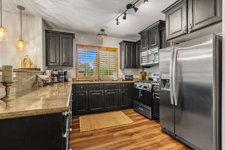 Your fully equipped kitchen features rich dark cabinetry, gleaming granite counters, and stainless steel appliancesâperfect for preparing meals while enjoying natural light streaming through the plantation shutters.