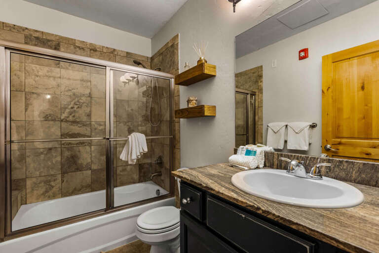 Your private bathroom offers a spacious walk-in shower with glass doors, plush towels, and warm rustic accents that create a relaxing retreat after your adventures.