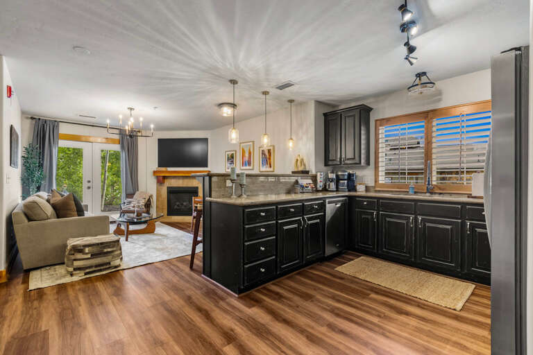 Your stylish open-concept living space features a fully-equipped kitchen with sleek black cabinetry and modern appliances flowing seamlessly into a cozy lounge area with a warm fireplace.