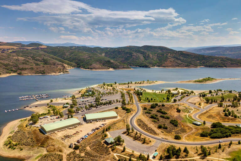 Aerial view of the property's stunning lakeside location, surrounded by rolling hills and natural landscape. Marina facilities and expansive grounds visible below.