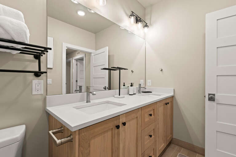 Step into your bright, modern bathroom with a double vanity, fresh white countertops, and warm wood cabinetry. Fluffy towels and thoughtful touches make freshening up a pleasure.