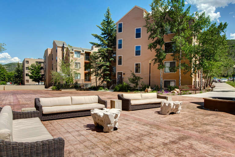 This property features comfortable outdoor lounge seating on a spacious brick patio, surrounded by mature trees and landscaped grounds with mountain views in the distance.