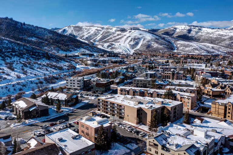 A charming mountain town nestled in a snowy valley, with ski slopes carving down distant peaks and cozy lodges dotting the landscape below.