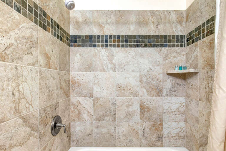Step into your beautifully tiled walk-in shower with elegant travertine and mosaic accents, stocked with complimentary amenities for your comfort.