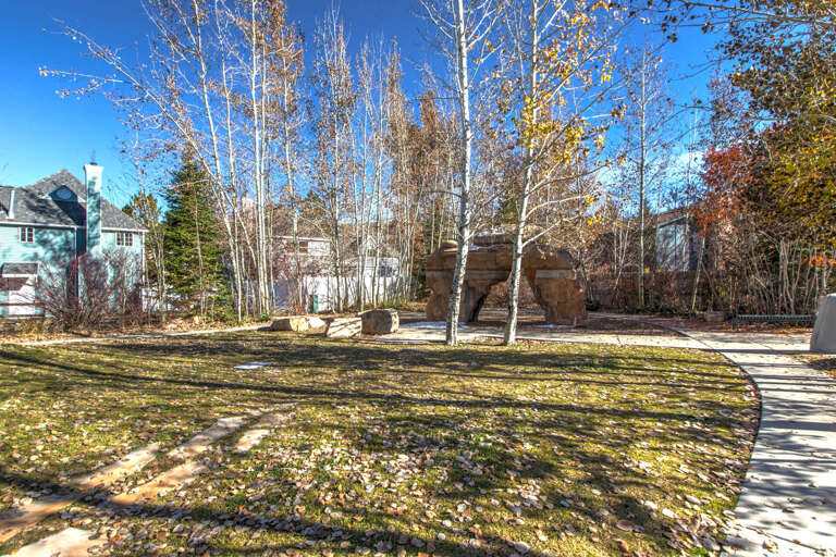 A spacious yard with mature birch trees and natural stone features, located in a peaceful residential neighborhood with mountain access nearby.