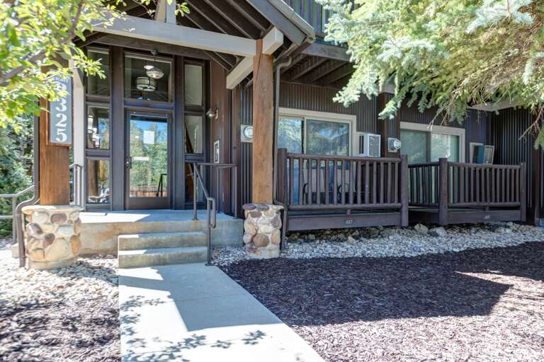 The property entrance features natural stone accents, modern wood and metal details, and welcoming outdoor spaces surrounded by mature trees and landscaping.