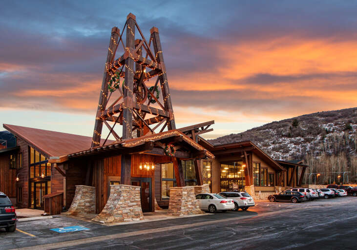 The property sits at the base of snow-dusted mountains, with a striking illuminated tower marking the entrance and parking conveniently located steps away.