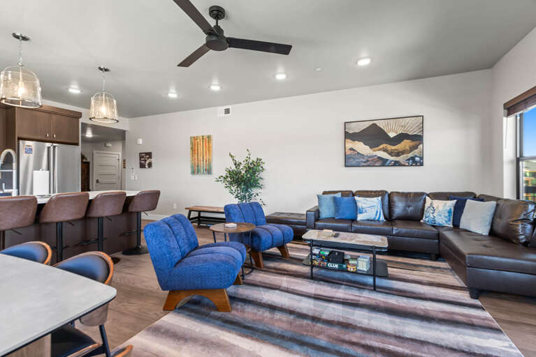 Settle into your open living area where a sleek leather sectional and vibrant blue chairs invite relaxation. The modern kitchen beckons just steps away, ready for your morning coffee or evening meals.