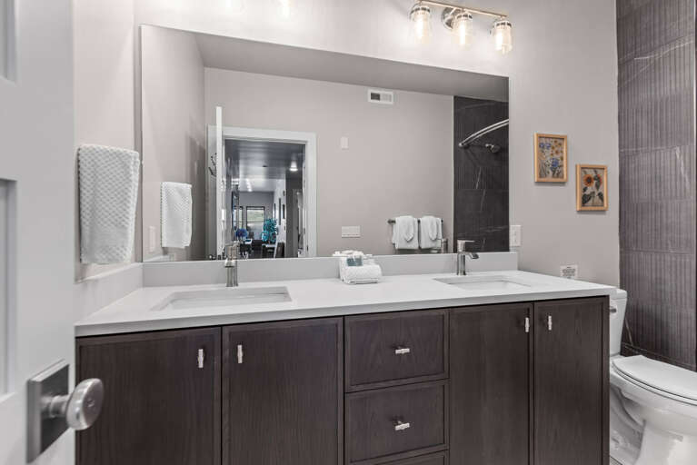 Freshen up in your modern bathroom with dual sinks, sleek dark cabinetry, and a spacious walk-in shower with elegant tile details.