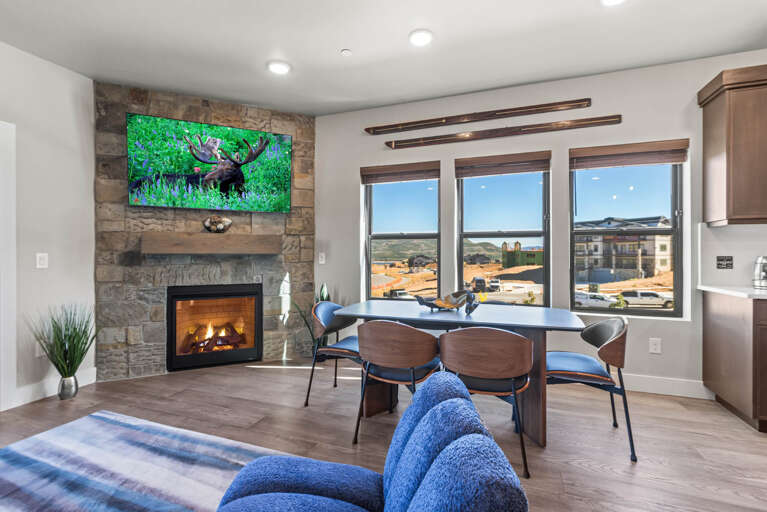 Step into your bright, open living and dining space where a warm fireplace and modern kitchen await. Through expansive windows, take in sweeping views of the surrounding landscape—mountains and open skies frame your everyday escape.