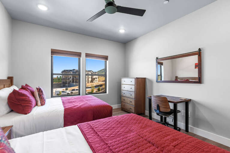 Two comfortable beds with vibrant linens welcome you to your serene retreat, complete with a ceiling fan, desk workspace, and hillside views framing your peaceful mountain getaway.