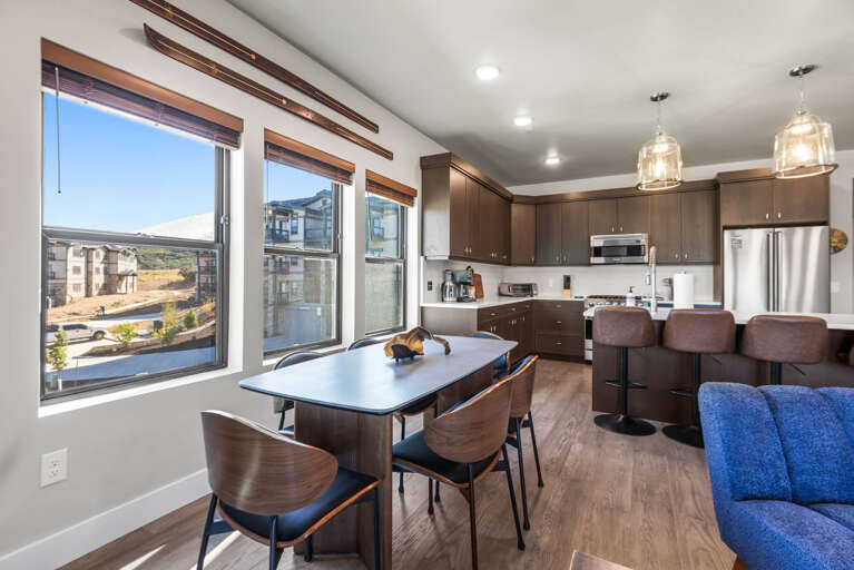 Settle into your open-concept space where modern meets cozy. Enjoy coffee at the sleek dining table, whip up a meal in your fully equipped kitchen, or relax on the plush blue sofa as natural light floods in through expansive windows.