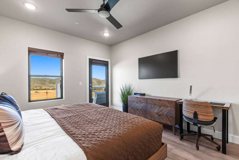 Unwind in your bright, modern bedroom with sweeping views of rolling hills and open skies. A cozy bed, sleek workspace, and ceiling fan create the perfect retreat for rest and relaxation.