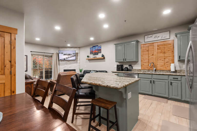 Gather around the spacious island where granite countertops and sage-green cabinetry create a warm, welcoming heart of the home. Your mornings here blend effortlessly with the open living space, perfect for conversation and connection.