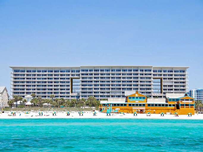 Beachfront Building With Turquoise Water And People On Sand