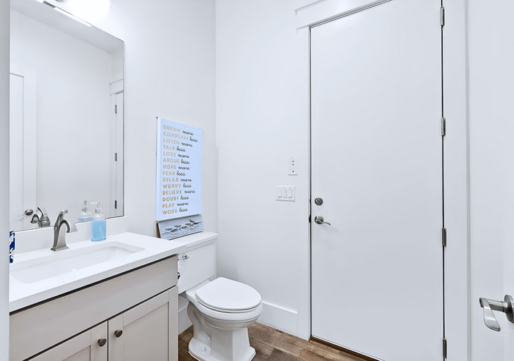 A modern bathroom with a white sink, mirror, and toilet. There is a motivational poster on the