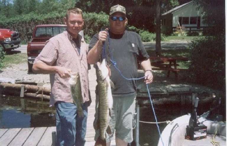 Two Men Holding Fish At A Lakeside Dock Two Men Holding Fish At A Lakeside Dock