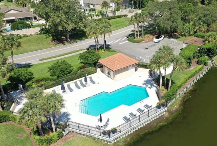 Aerial View Of A Pool Beside A Building, Surrounded By Greenery And Water