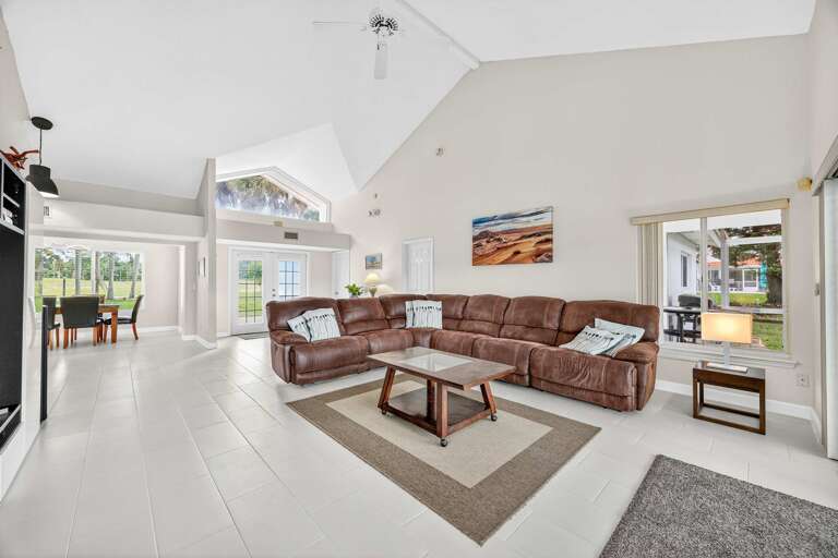 Bright, Breezy Living Room With Vaulted Ceiling, Leather Seating, And Large Windows Showing Lush Lawn