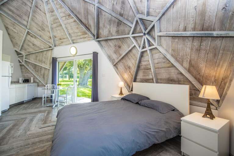 Bed Beneath Geometric Beams, Broad Windows View Verdant Vista