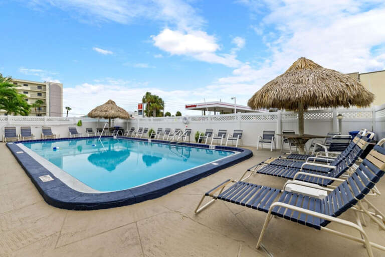 Inviting outdoor pool with lounge chairs and shaded tiki seating, perfect for relaxing and enjoying the Florida sunshine.