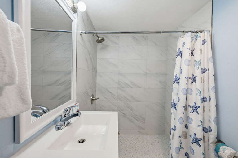 Updated coastal bathroom with spacious walk-in shower, modern tile, vanity, and fresh towels for a comfortable beach getaway.