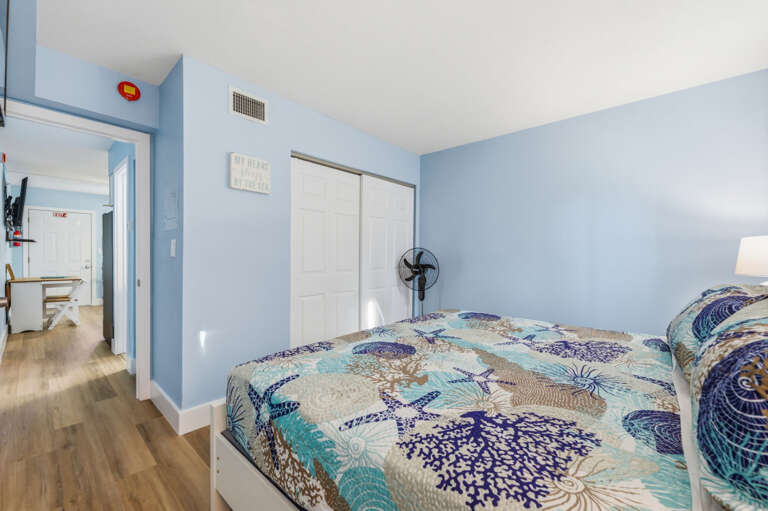 Spacious coastal bedroom with comfortable bed, Smart TV, closet storage, and bright beach-inspired décor.