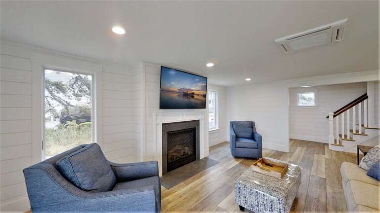 Bright Living Space With Blue Chairs, Television Above Fireplace, Hardwood Floors, And Staircase